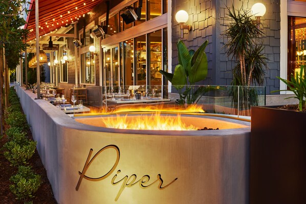 An outdoor seating area with a fire feature labeled "Piper," tables, chairs, and potted plants.