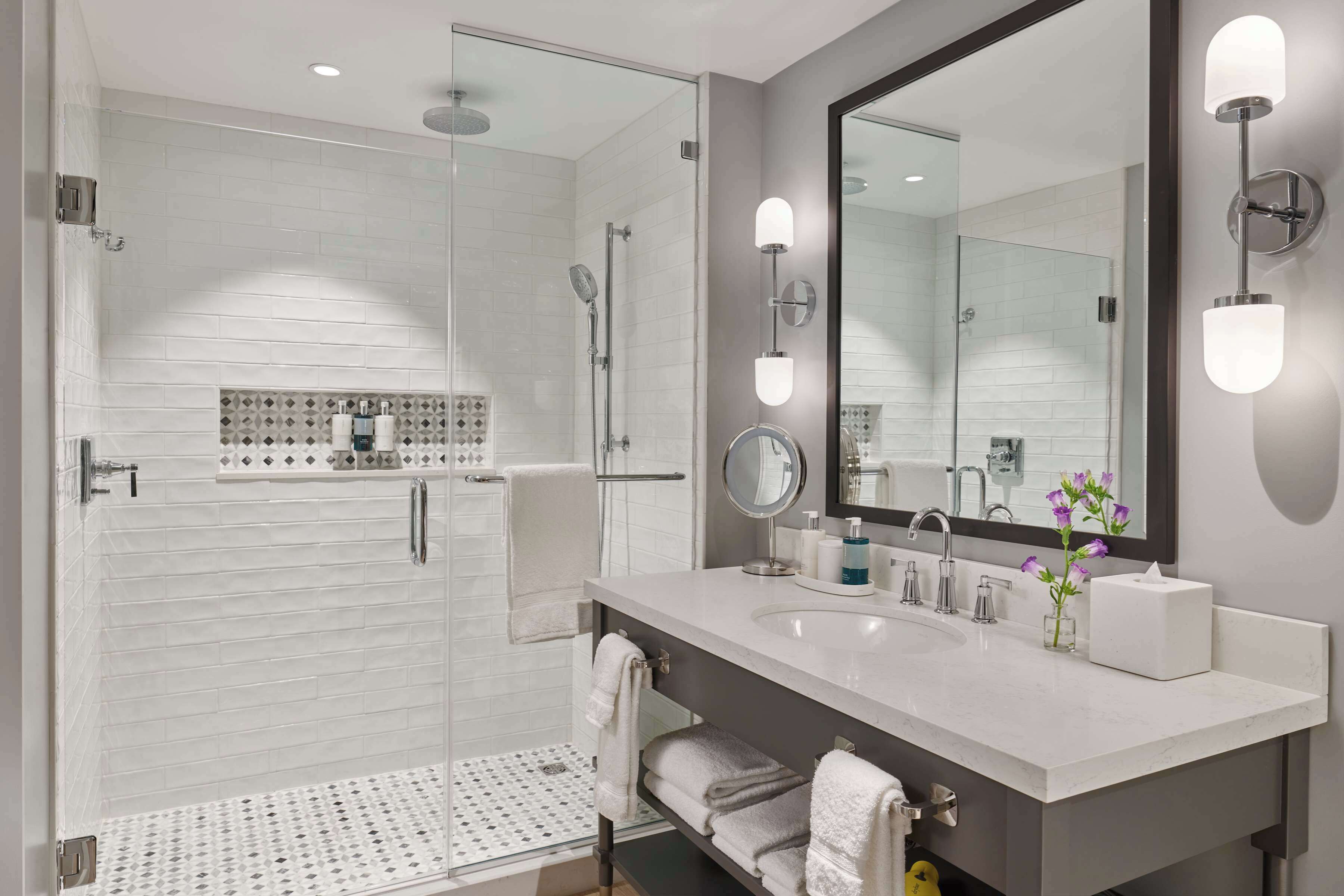 A modern bathroom with a glass-enclosed shower, a large mirror, and a white vanity with a sink and towel rack.