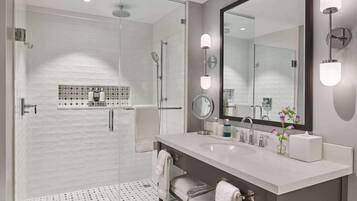 Une salle de bain moderne avec une douche à parois de verre, un grand miroir et un meuble-lavabo blanc doté d’un évier et d’un porte-serviettes.