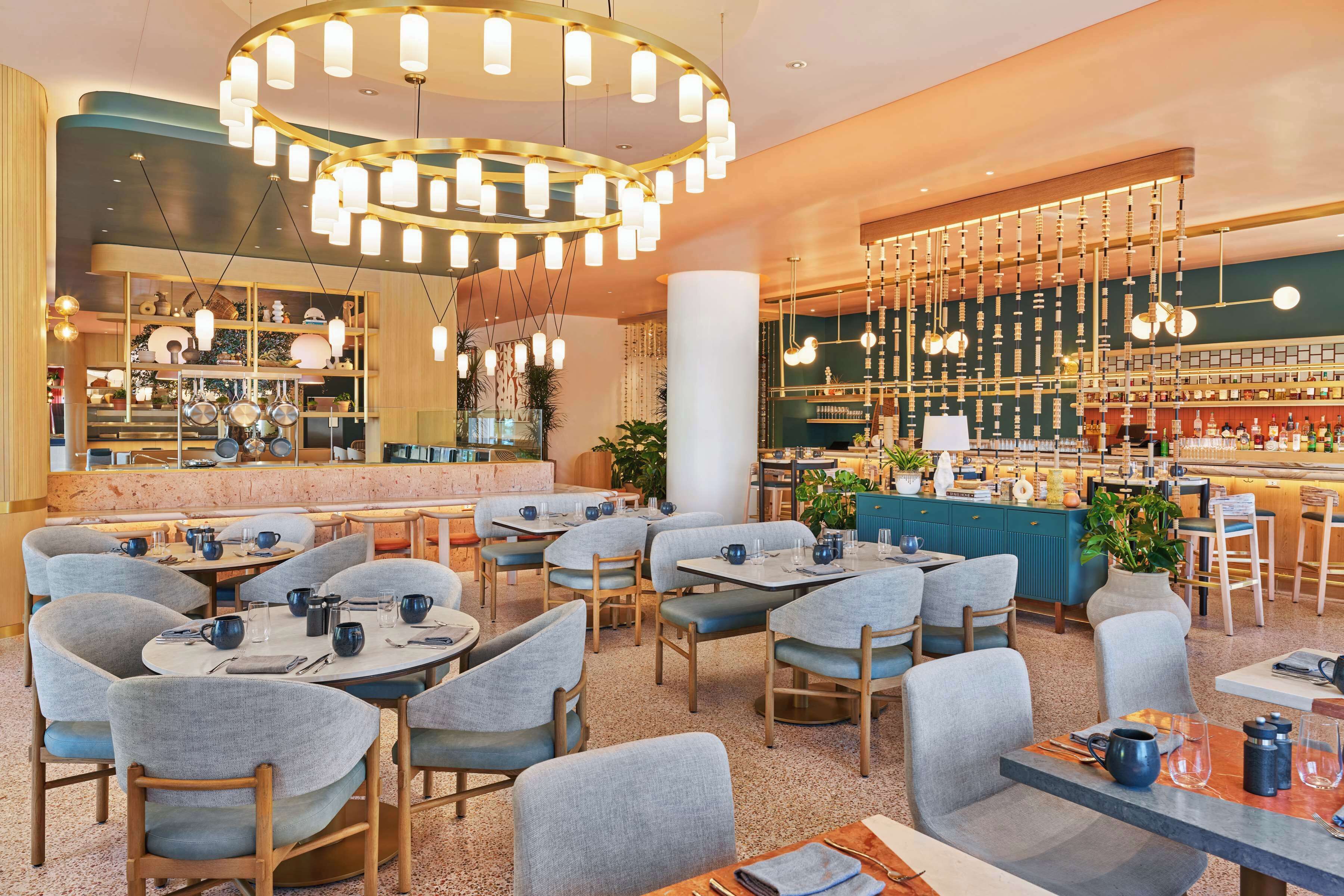 Um restaurante moderno com mesas redondas, cadeiras estofadas cinzentas e um bar com prateleiras cheias de garrafas.