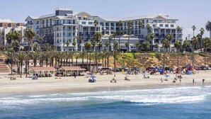 A beachfront hotel with multiple floors, palm trees, and beach amenities. - The Seabird Ocean Resort & Spa, Part of Destination Hotel by Hyatt (Oceanside)