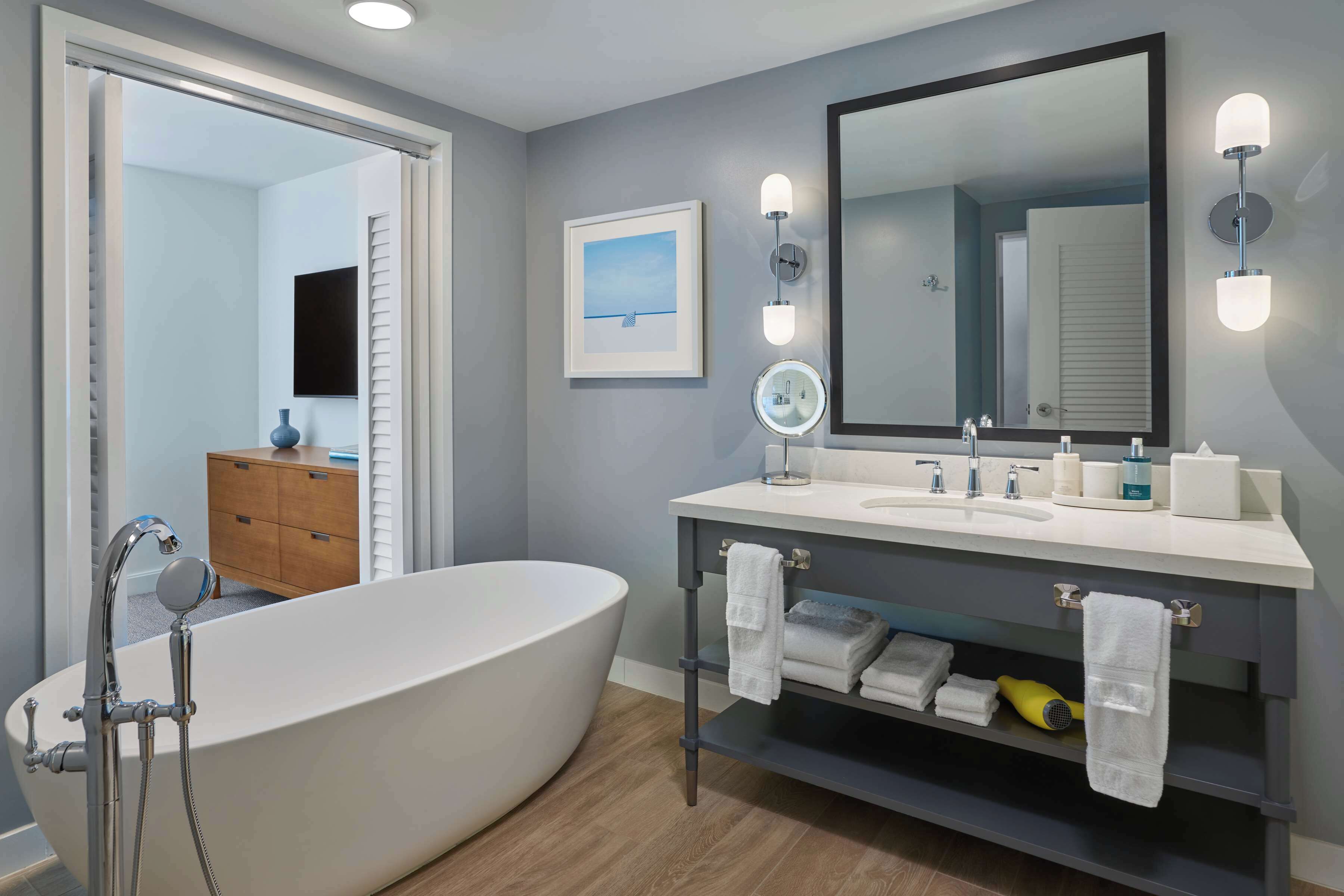 A modern bathroom with a freestanding bathtub, a vanity with a mirror, and a framed picture on the wall.