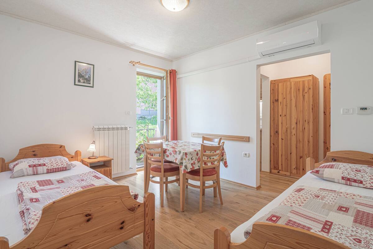 A bedroom with two wooden beds, a dining table with chairs, a radiator, and a door leading outside.
