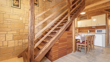 A wooden staircase leading to a kitchen area with stone walls and a dining table set.