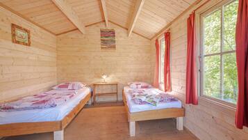 A cabin with two wooden beds, a small table with a lamp, and a window with curtains.