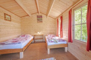 A cabin with two wooden beds, a small table with a lamp, and a window with curtains.