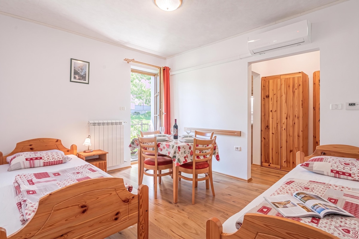 A room with two wooden beds, a dining table with chairs, a radiator, and a window with curtains.