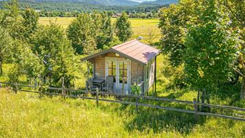 A small wooden cabin with a red roof, surrounded by lush greenery and a fenced area.