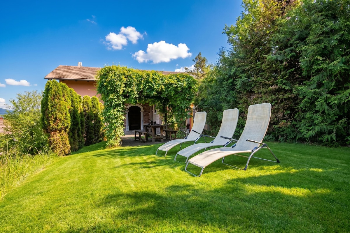 A house with a covered patio, three lounge chairs, and a well-maintained lawn.