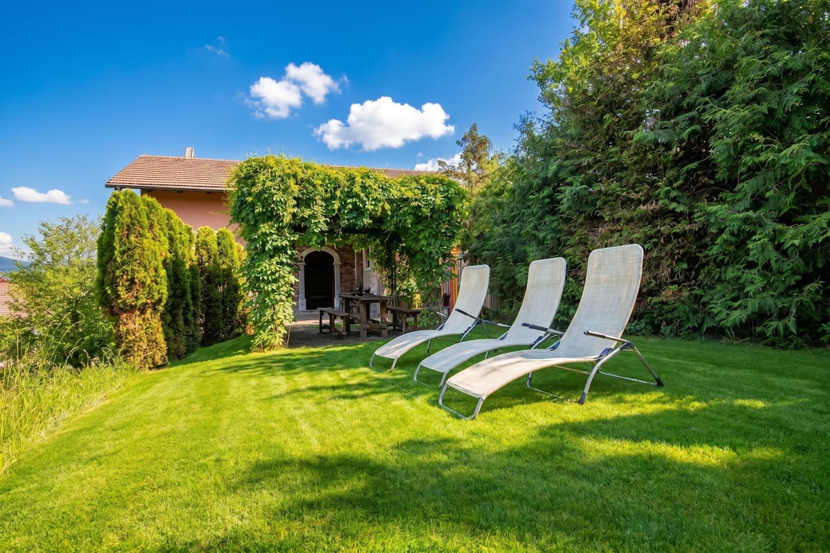 A house with a covered patio, three lounge chairs, and a well-maintained lawn.