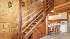 A wooden staircase leading to a kitchen area with stone walls and a dining table set.
