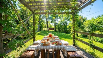 An outdoor wooden pergola with a picnic table set up for a meal.