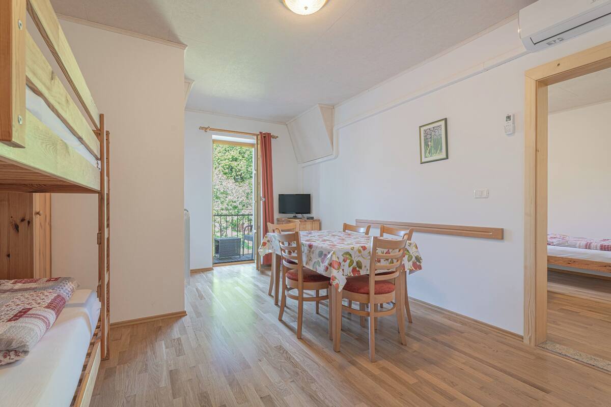 A room with a bed, a dining table with chairs, a television, and a window with curtains.