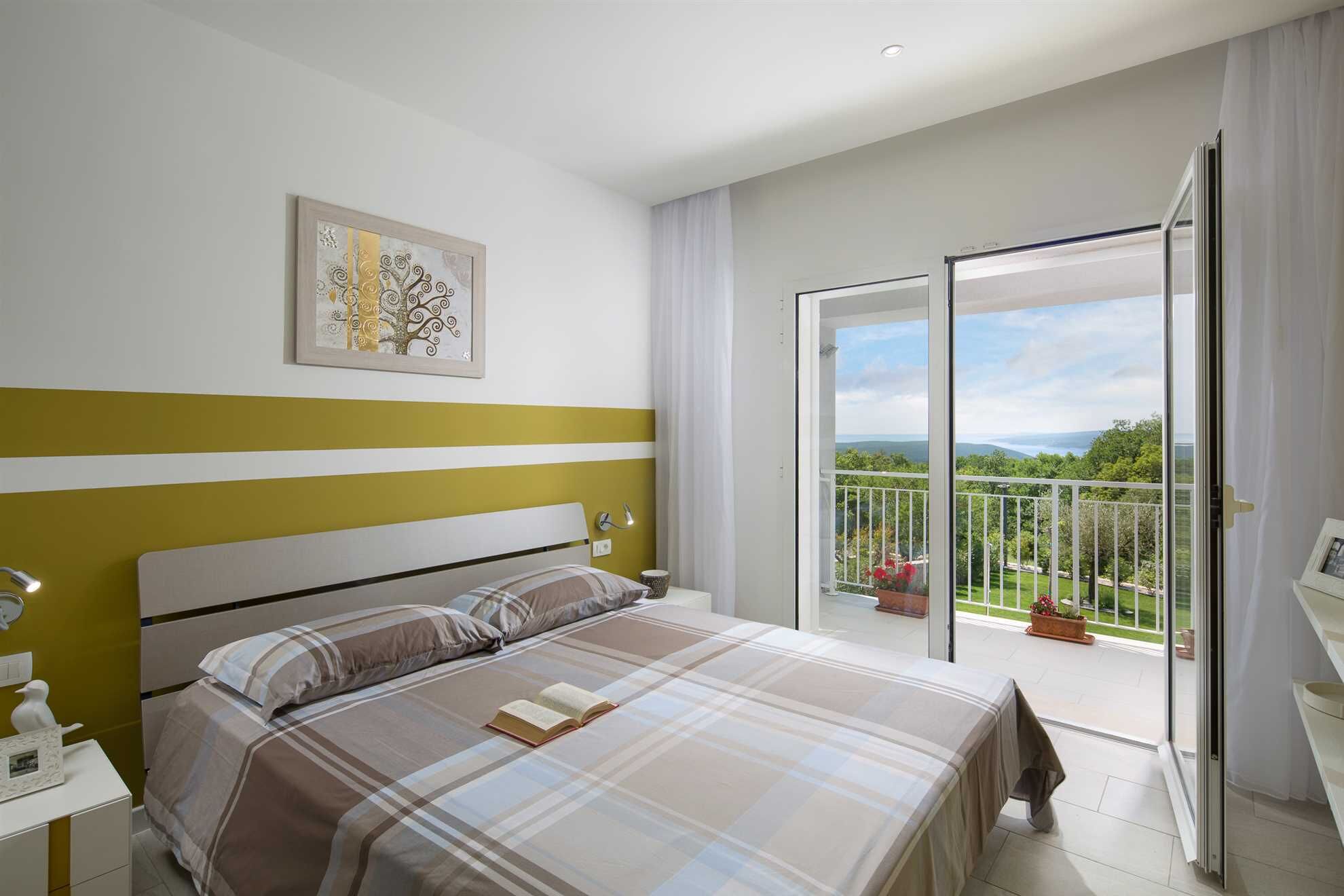 Une chambre à coucher comprenant un lit, une table de chevet, une commode, une fenêtre et un balcon avec vue.