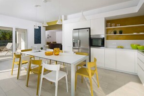 A modern kitchen with white cabinets, a stainless steel refrigerator, and a dining area with a white table and yellow chairs.