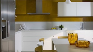 A modern kitchen with white cabinetry, a stainless steel refrigerator, a yellow accent wall, and a dining area with a white table and chairs. - Villa Deborah (Raša)