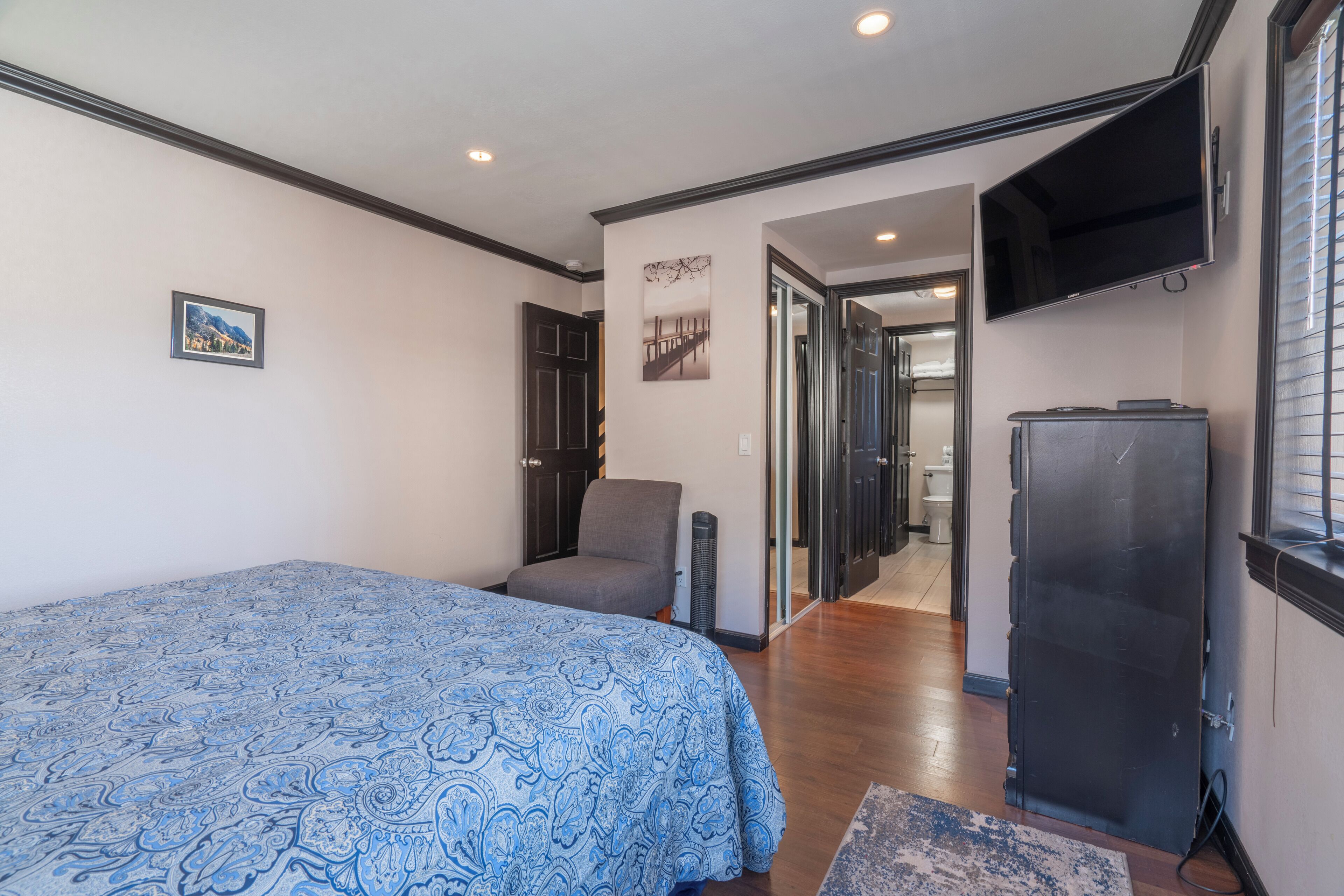 A bedroom with a bed, a chair, a TV, and a refrigerator.