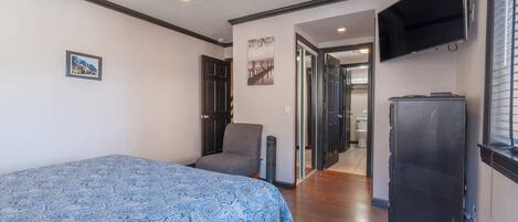 A bedroom with a bed, a chair, a TV, and a refrigerator.