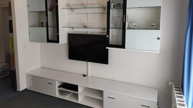A modern entertainment unit with a flat-screen TV, two mirrored cabinets, and shelves for storage.
