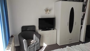 A hotel room with a grey armchair, a TV on a white cabinet, a wardrobe, and a radiator.