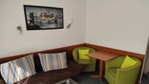 A corner seating area with a brown sofa, two green armchairs, and a glass-top coffee table.