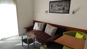A modern living room with a brown sofa, striped pillows, a glass coffee table, a wooden side table, and a green armchair.