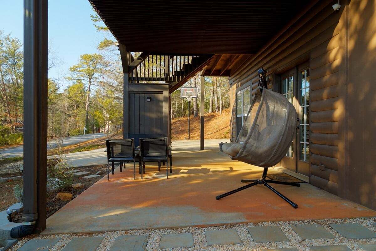 A log cabin with a covered porch, outdoor seating, and a hanging chair.