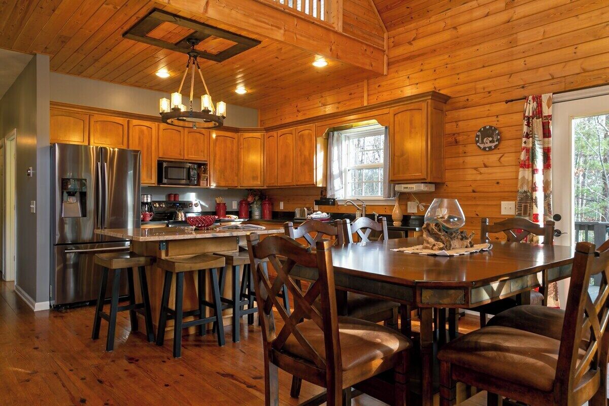 A wooden cabin interior with a kitchen, dining area, and a large window.
