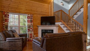 Ein gemütliches Wohnzimmer mit Kamin, Ledersofas und einer Wendeltreppe.