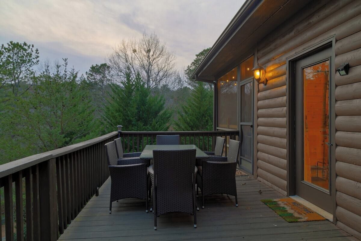 A wooden deck with a table and chairs, a door with glass panels, and a view of trees.