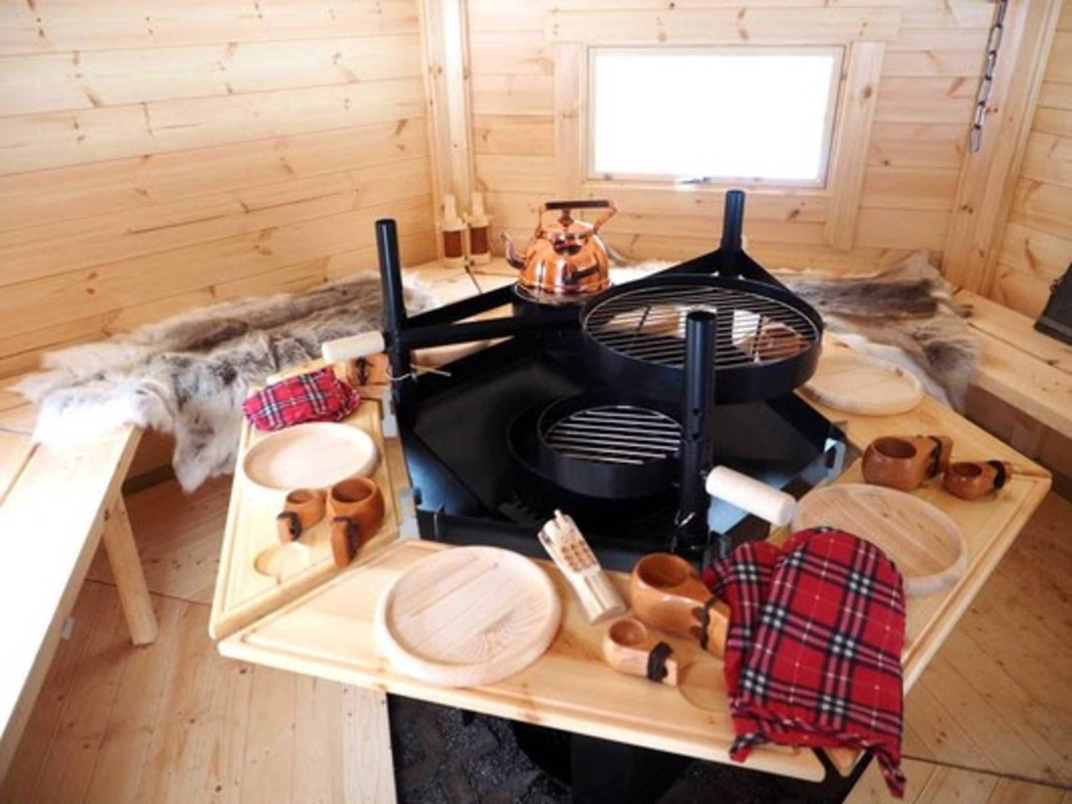 Un intérieur en bois avec une table dressée pour le repas, un barbecue noir et un banc recouvert de fourrure.