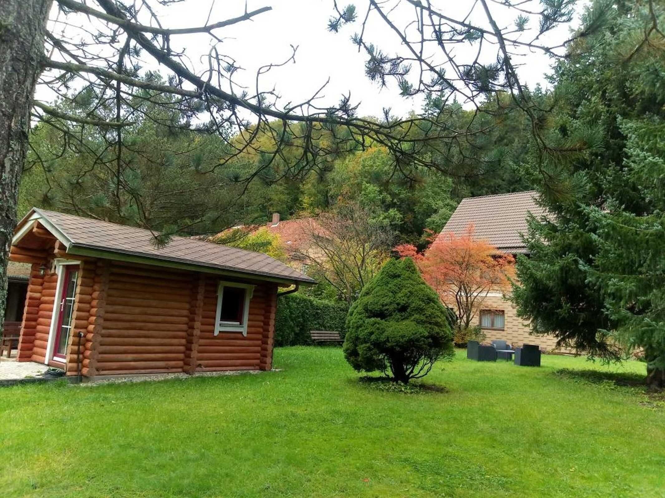 Eine Blockhütte mit einer kleinen Veranda und einem Fenster, umgeben von einem Rasen und Bäumen.
