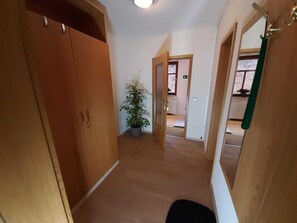 A hallway with wooden doors, a potted plant, and a view into another room.