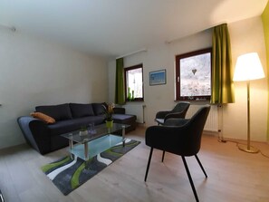 A living room with a sofa, a glass coffee table, a chair, a lamp, and a view of a snowy landscape through the windows.