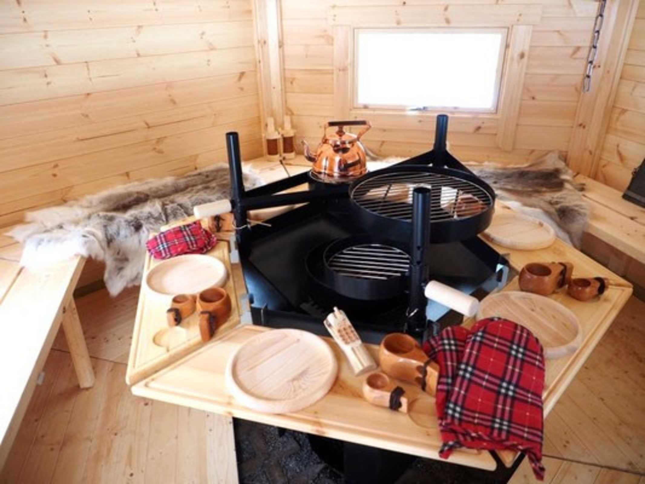 A wooden interior with a table set for dining, a black grill, and a fur-covered bench.