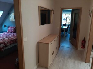 A bedroom with a bed, a bedside table, a dresser, and a mirror. There is a hallway leading to a dining area with a table and chairs. - Staufenberg Vacation Rental - House in Wolfsbach - Vacation Apartments (Walkenried)