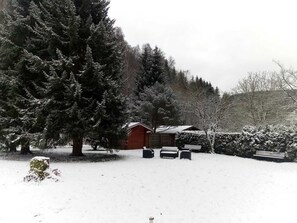 A snow-covered landscape with a red cabin, a large evergreen tree, and a bench. - Staufenberg Vacation Rental - House in Wolfsbach - Vacation Apartments (Walkenried)