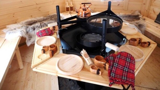 En inredning med träpanel, ett bord dukat för middag, en svart grill och en bänk klädd med fäll.