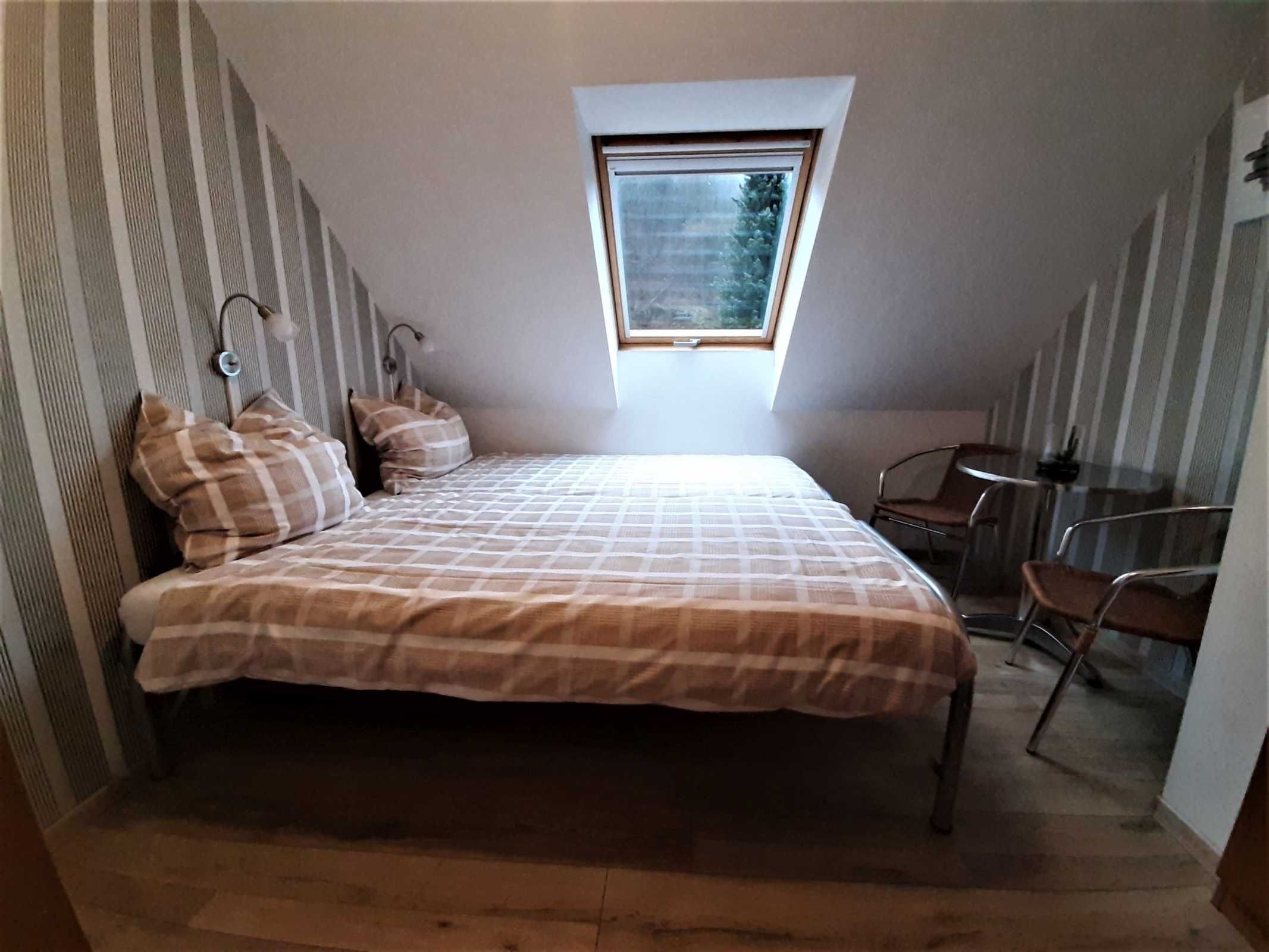 A bedroom with a bed, a desk, a chair, and a skylight.