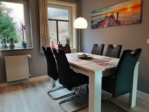 A dining area with a table, chairs, a painting, a window with curtains, and a radiator.