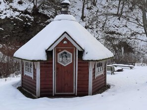 Pieni puinen mökki, jonka katto on lumen peitossa ja jossa on kuusikulmainen ikkuna.