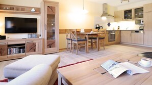 Een moderne woonkamer met een flatscreen televisie, een bank, een eettafel met stoelen en een keuken met kasten en apparatuur.