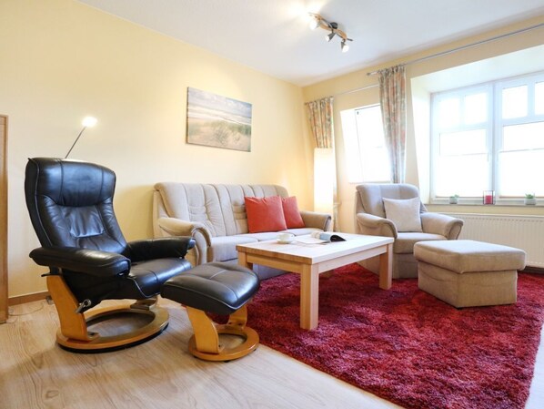 Ein Wohnzimmer mit einer Couch, zwei Sesseln, einem Couchtisch und einem roten Teppich.