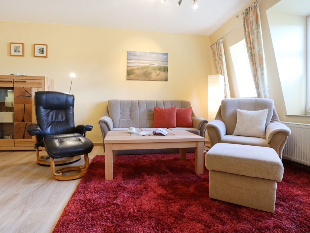A living room with a red carpet, a grey sofa, a black leather chair, and a beige armchair.