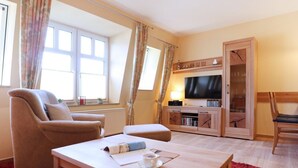 Een woonkamer met een bank, een bijzettafeltje met een kopje, een televisie en een houten kast.