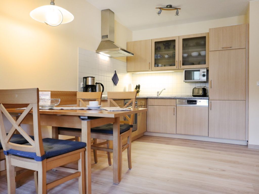A modern kitchen with wooden cabinets, a dining table with chairs, and a microwave.