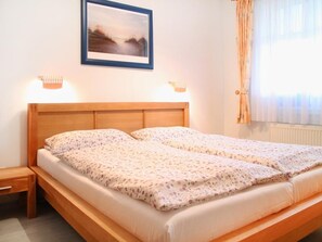 Ein Doppelbett mit Holzfußteil, zwei Nachttische, ein gerahmtes Bild an der Wand und ein Fenster mit Vorhängen.