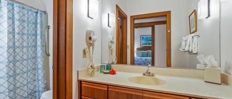 Ein Badezimmer mit einem Holzbadschränken, einem großen Spiegel und einer Dusche mit einem Vorhang mit geometrischem Muster.