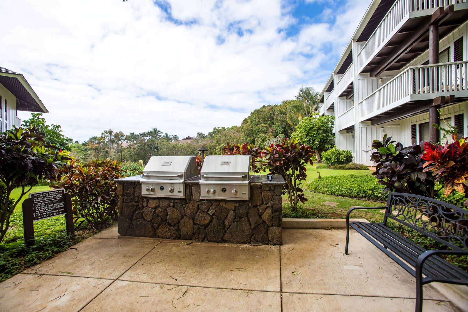 An outdoor barbecue area with two grills, a stone wall, and a bench.