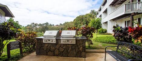 An outdoor barbecue area with two grills, a stone wall, and a bench.